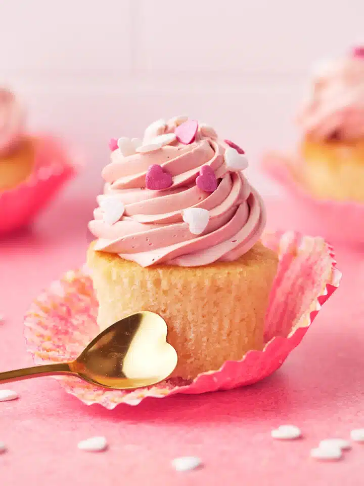 Valentines cupcakes on a pink background with white heart sprinkles all around.