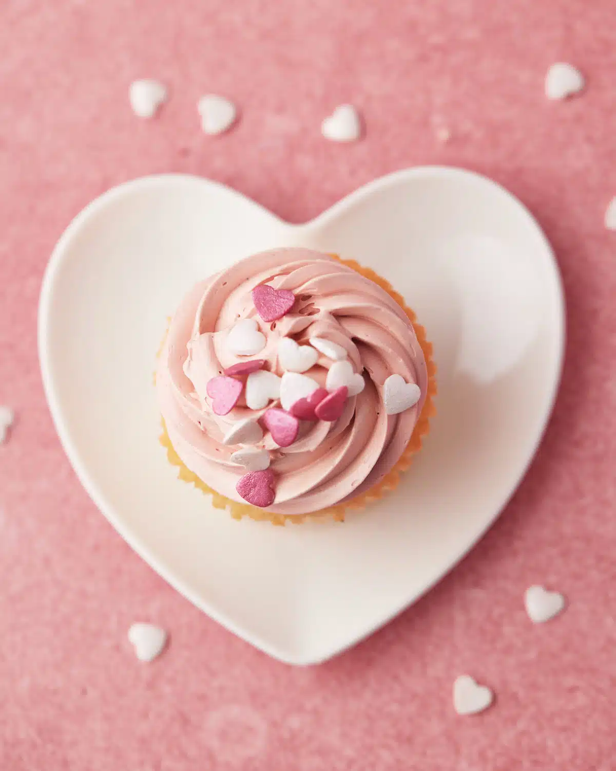 Valentines cupcake with pink frosting on a heart shaped plate, shot from above. 