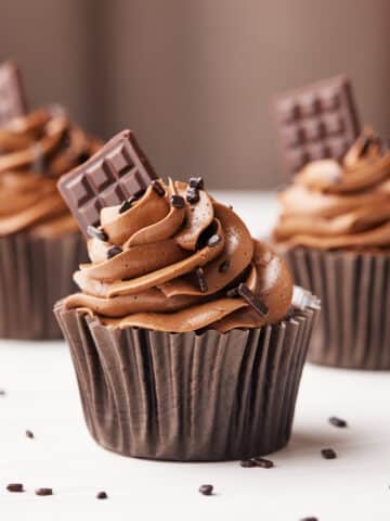 Chocolate cupcakes in brown paper cases with chocolate buttercream frosting and a mini chocolate bar sticking out the side.