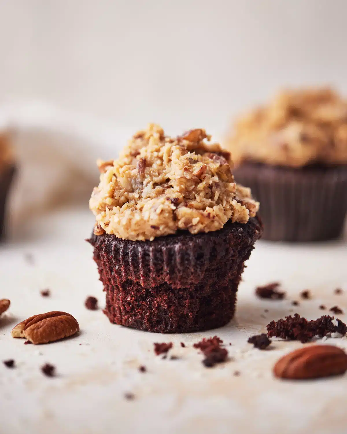 German chocolate cupcake on a table with chopped pecans all around it. 