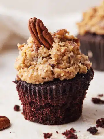 Single german chocolate cupcake with coconut pecan frosting and a single pecan perched on top.