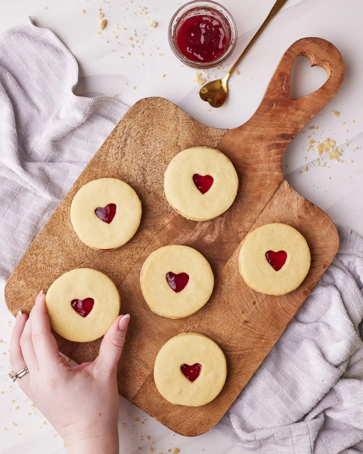Homemade Jammie Dodgers on a wooden board, one being picked up for a bite.