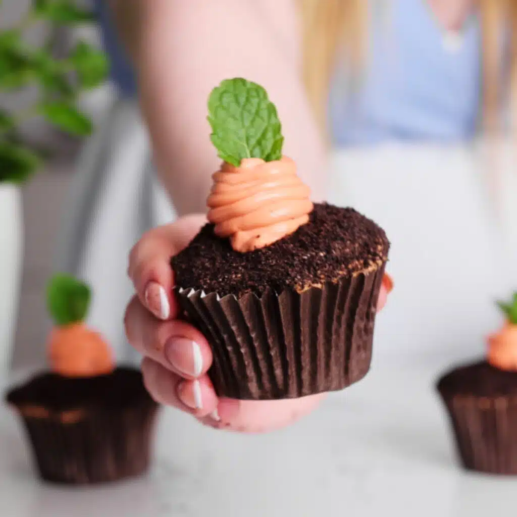 Chocolate cupcake with an orange cheesecake carrot piped in the middle and a sprig of mint as the leaves.