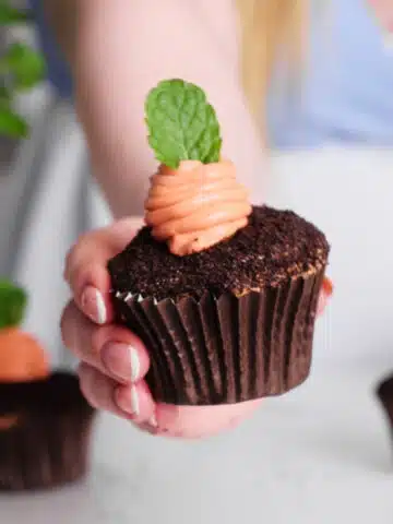 Chocolate cupcake with an orange cheesecake carrot piped in the middle and a sprig of mint as the leaves.