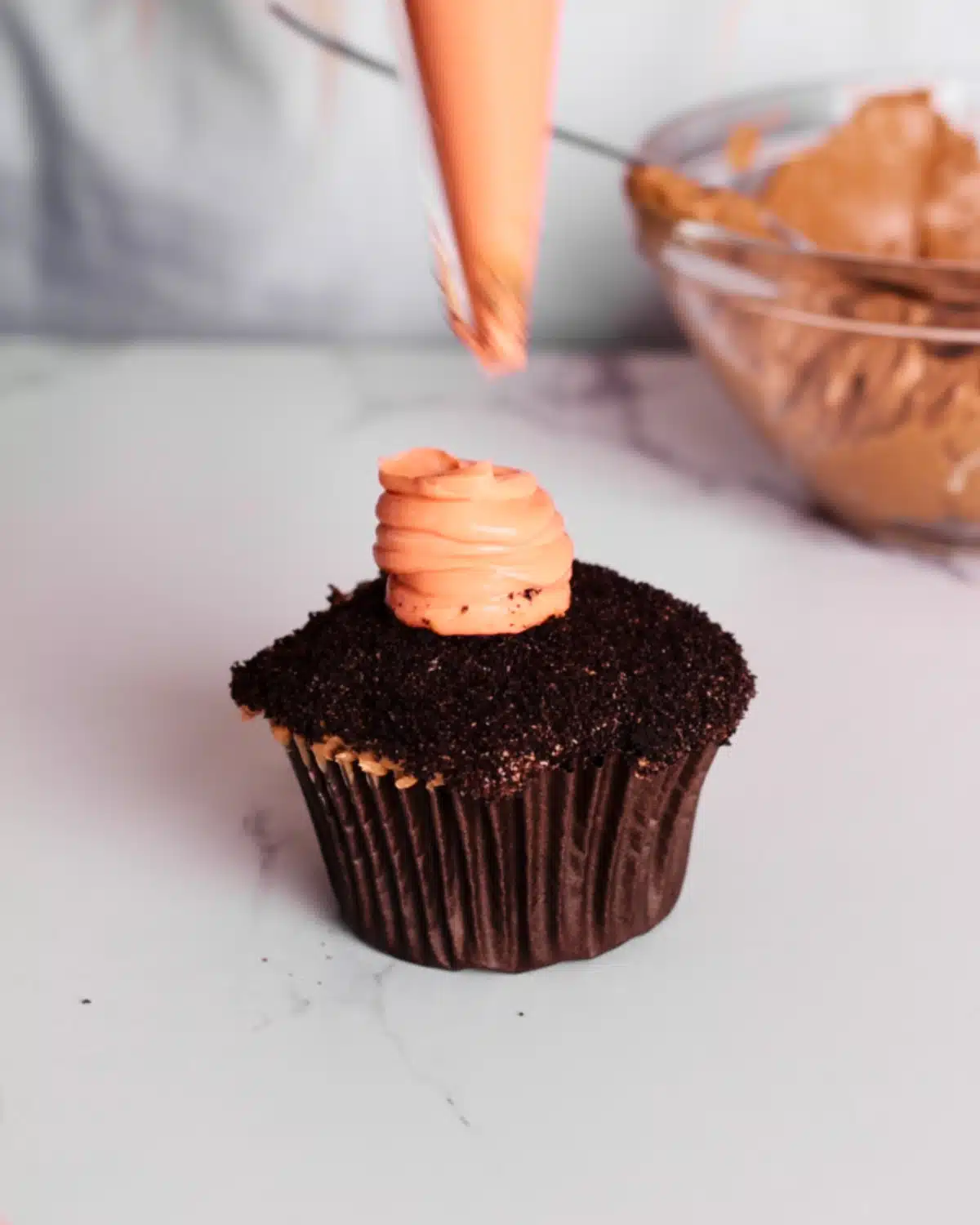 Orange colored cheesecake mixture being piped onto a chocolate cupcake to look like a carrot to make carrot patch cupcakes. 