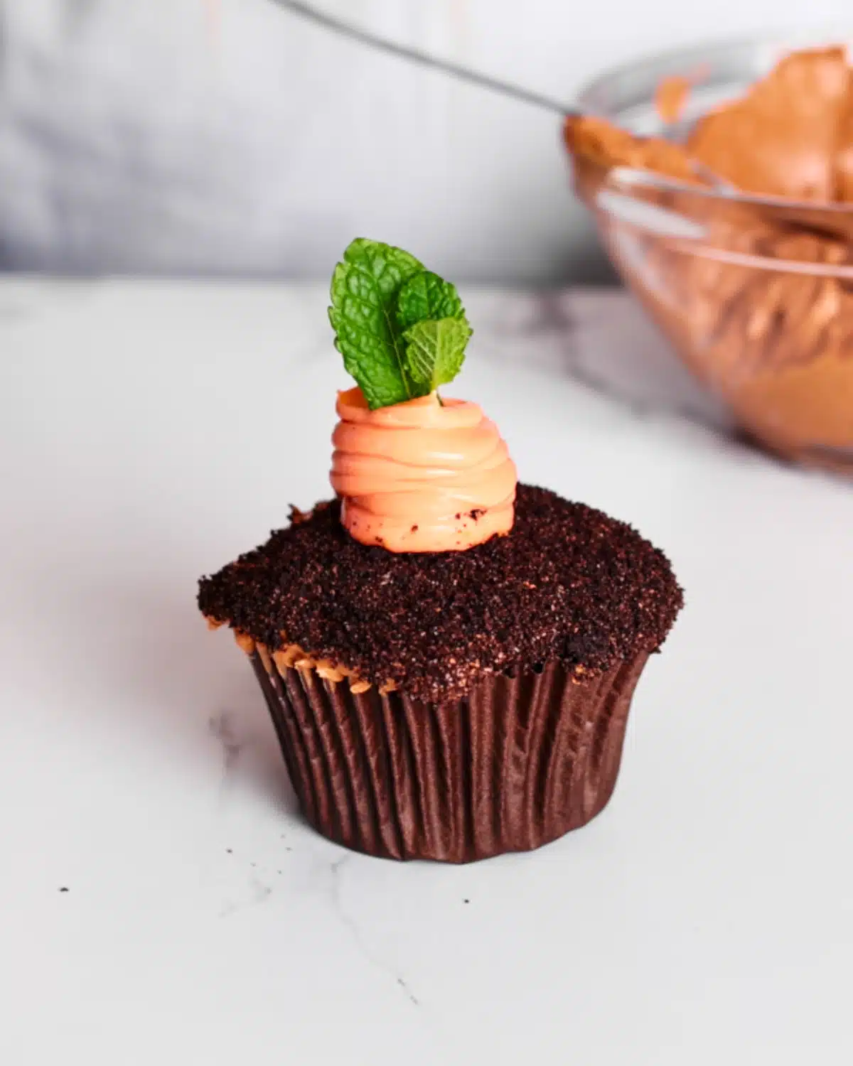 Chocolate cupcake with an orange cheesecake carrot piped in the middle and a sprig of mint as the leaves.