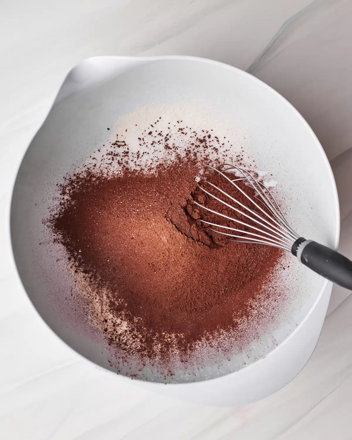 Mixing dry ingredients, including flour, sugar, and cocoa powder, together in a large white bowl to make chocolate cupcakes. 