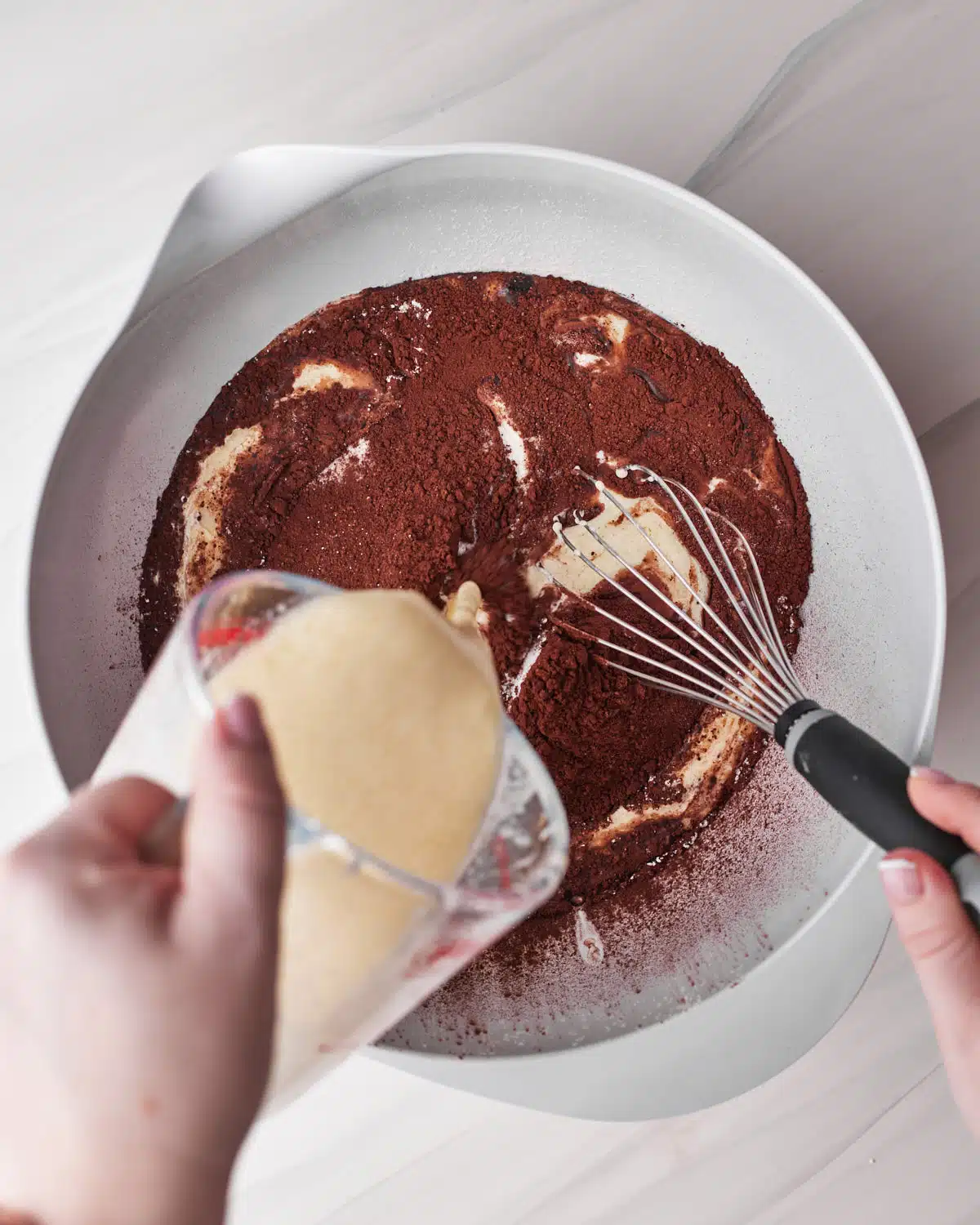 Pouring a jug of wet ingredients into dry ingredients to make chocolate cupcakes. 