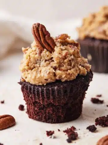 Single german chocolate cupcake with coconut pecan frosting and a single pecan perched on top.
