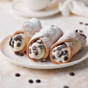 Three chocolate chip cannoli on a plate with homemade cannoli filling.