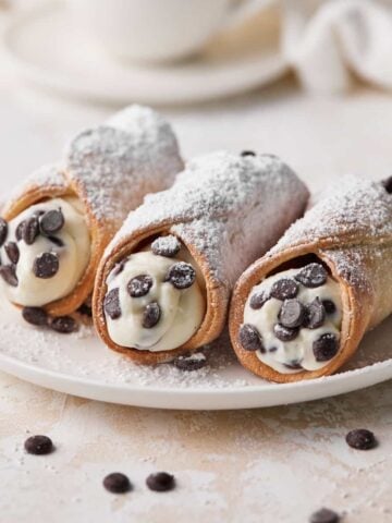 Three chocolate chip cannoli on a plate with homemade cannoli filling.
