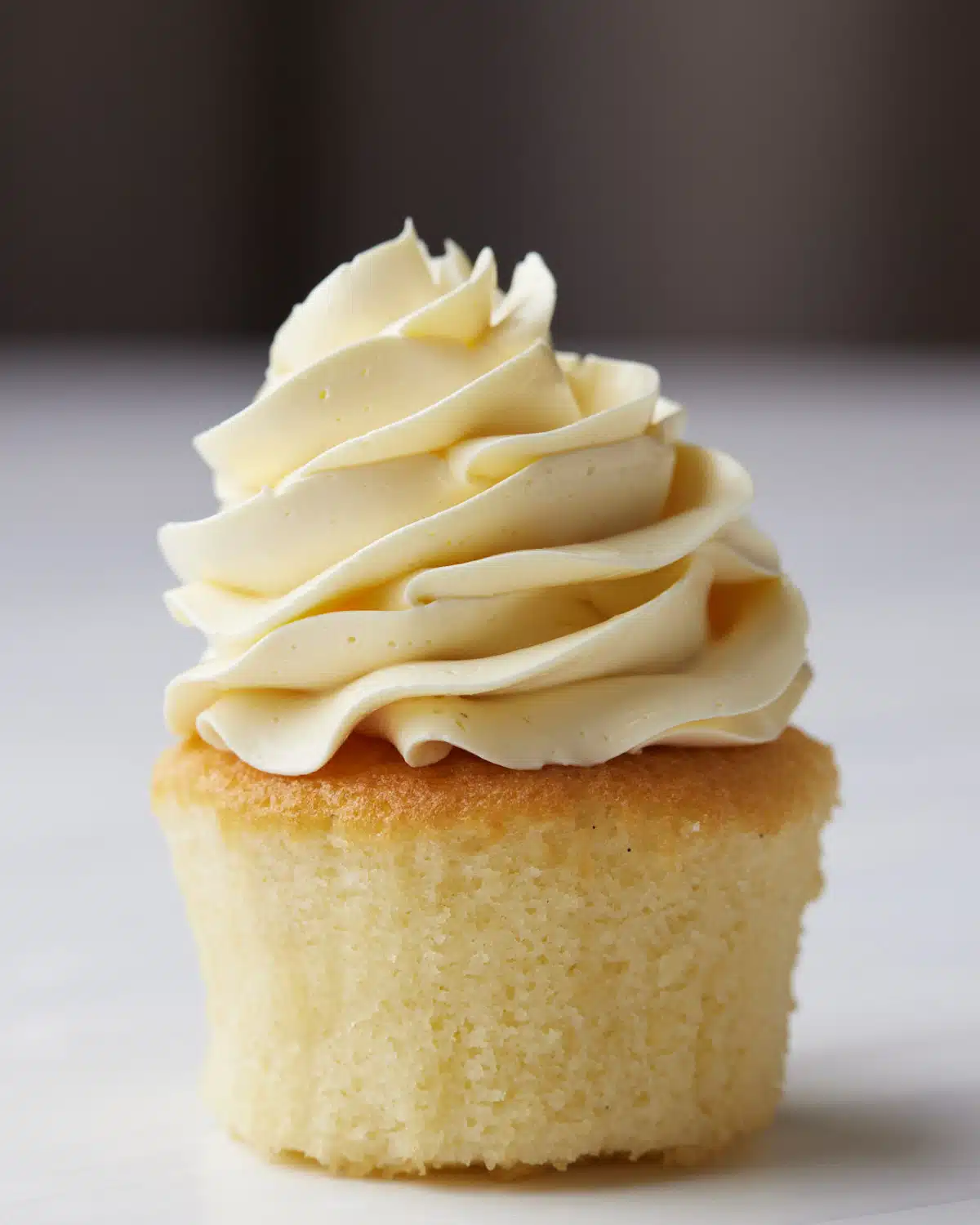 French buttercream piped in a swirl on top of a vanilla cupcake.