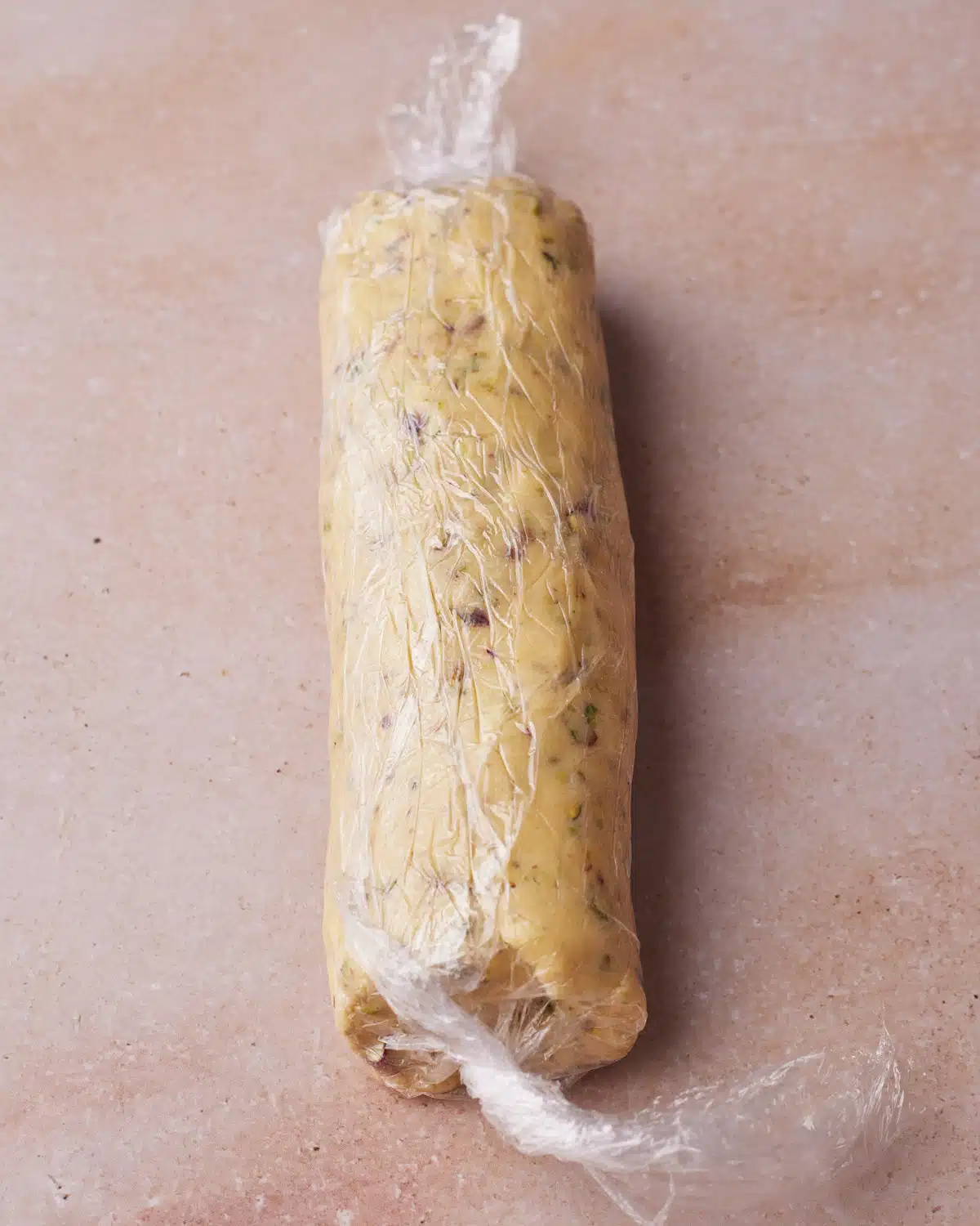 Pistachio shortbread dough rolled into a log and wrapped in plastic wrap to make slice-and-bake pistachio shortbread cookies.