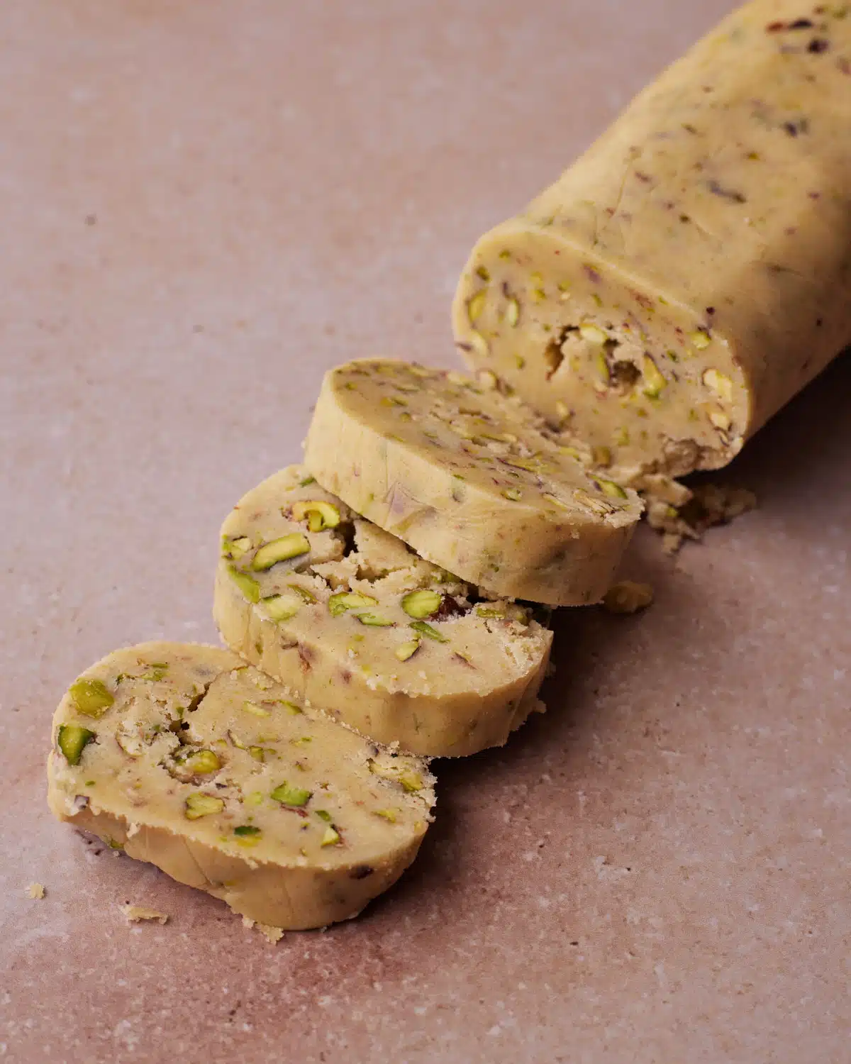 Log of pistachio shortbread dough being sliced into rounds before baking.