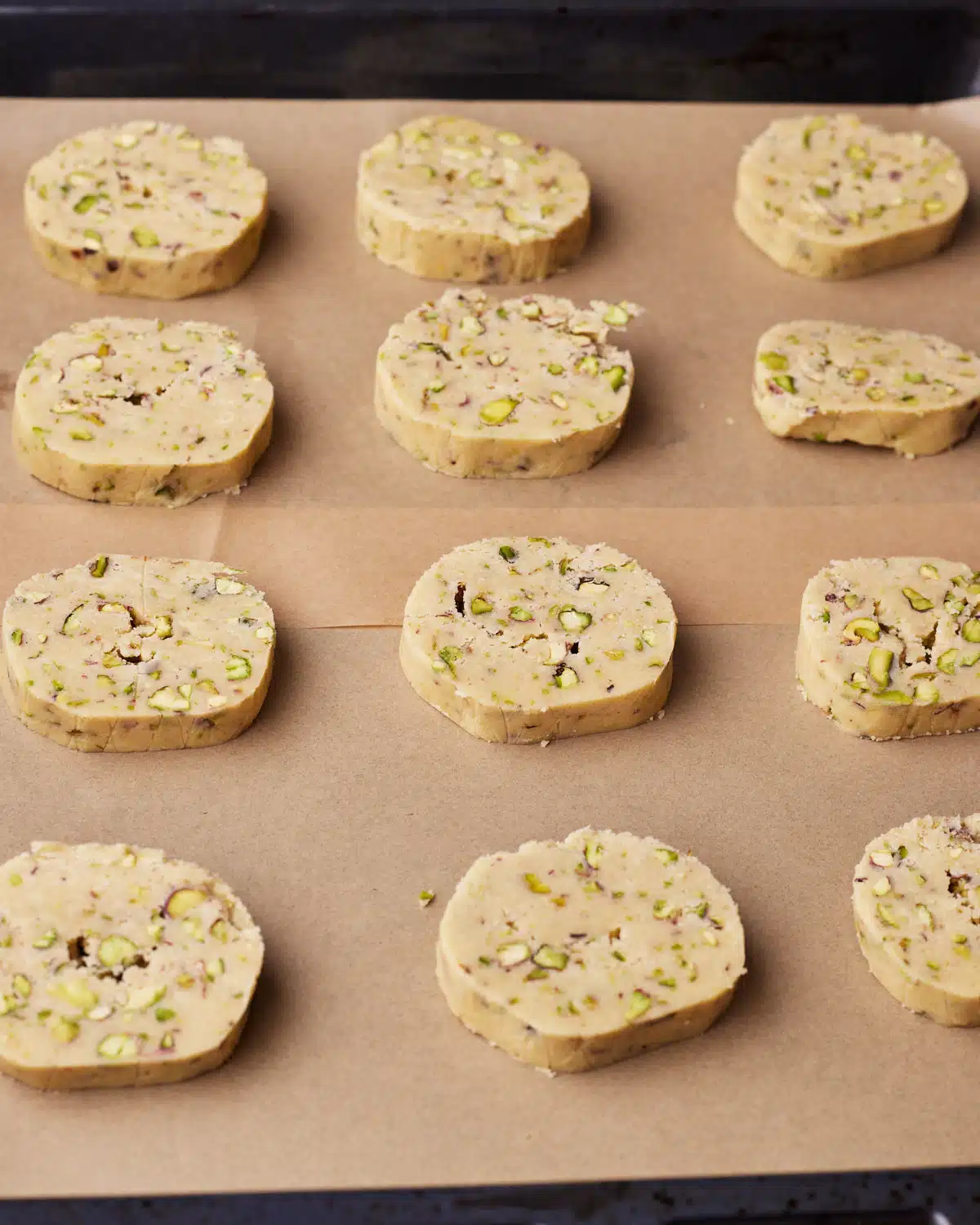 Unbaked rounds of pistachio shortbread dough on a baking sheet, ready to be baked.