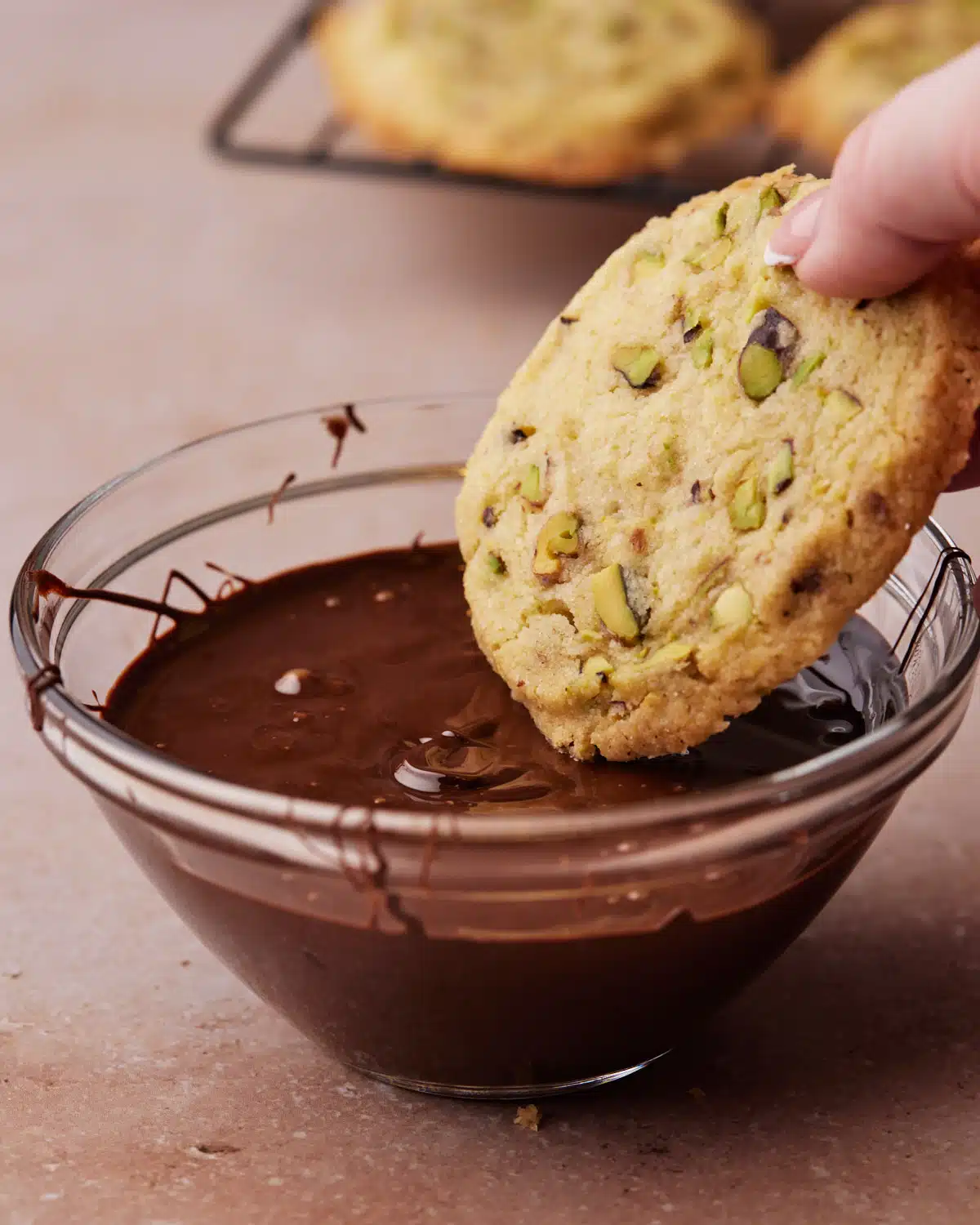 Pistachio Shortbread cookie being dipped in a bowl of dark chocolate.