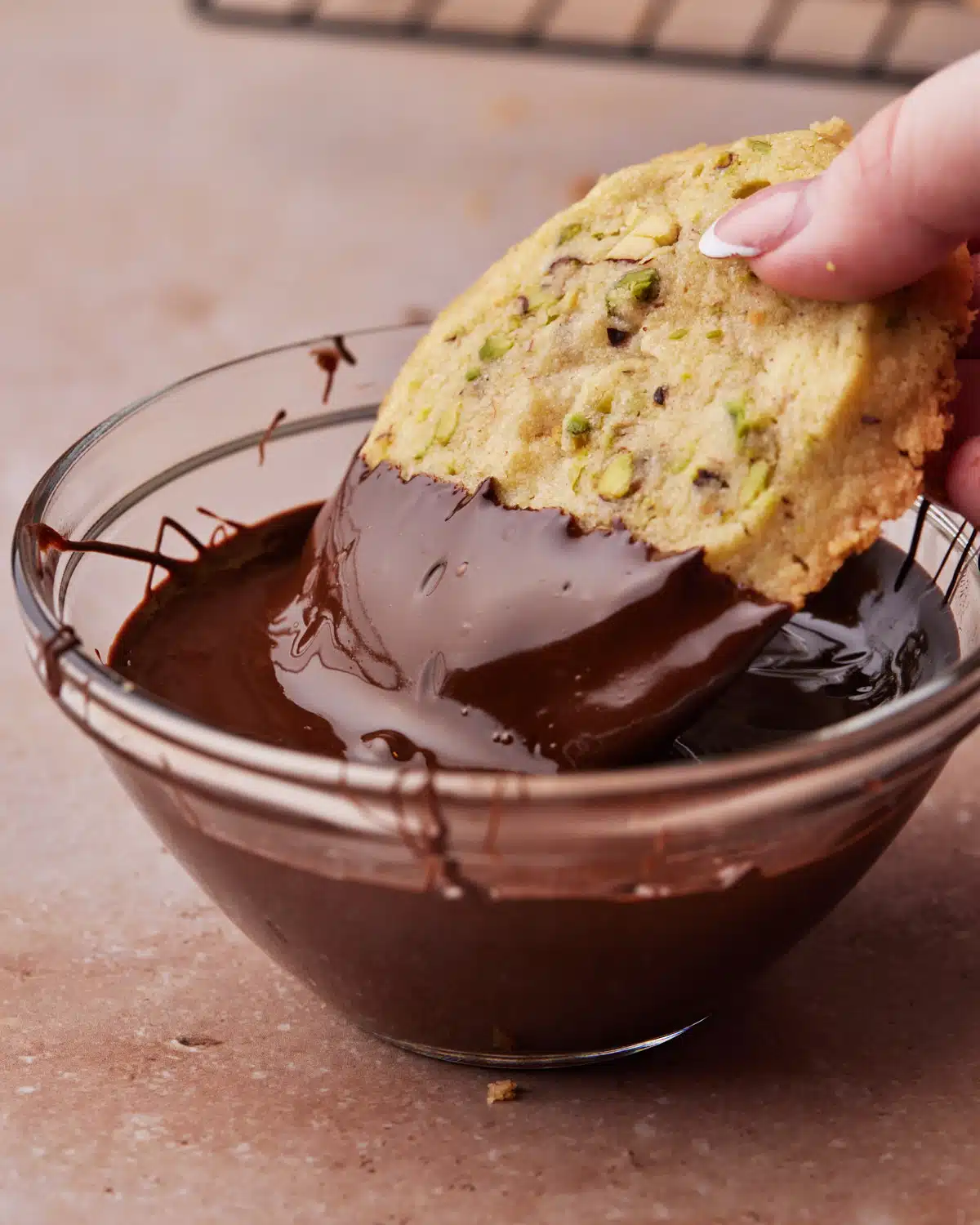 Pistachio Shortbread cookie being dipped in a bowl of dark chocolate.