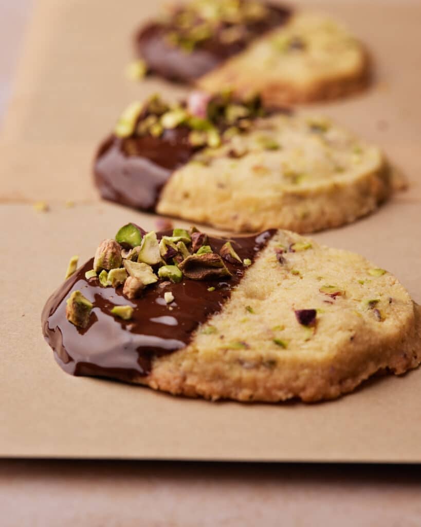Pistachio shortbread cookie that has just been dipped in dark chocolate and sprinkled with pistachios.
