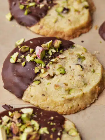 Round pistachio shortbread cookies in a row, dipped in chocolate and topped with chopped pistachios.