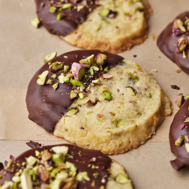 Round pistachio shortbread cookies in a row, dipped in chocolate and topped with chopped pistachios.