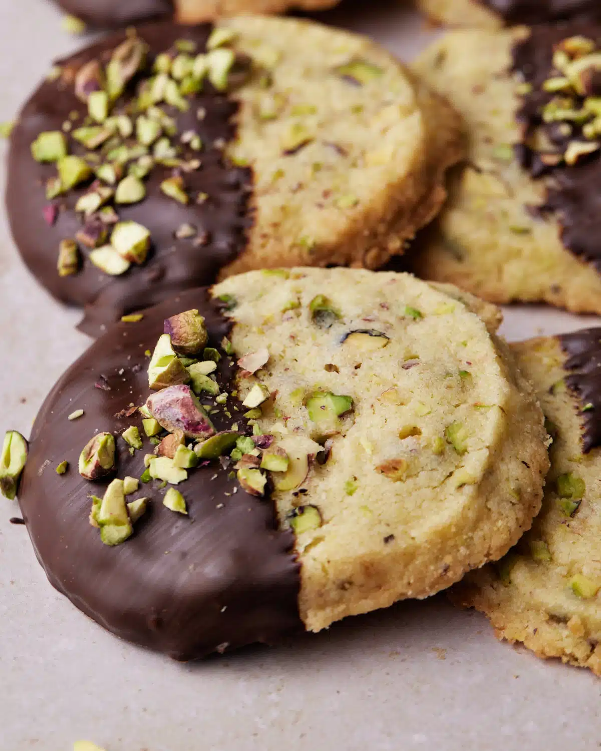 Close up of pistachio shortbread cookies which are half dipped in chocolate and topped with chopped pistachios.