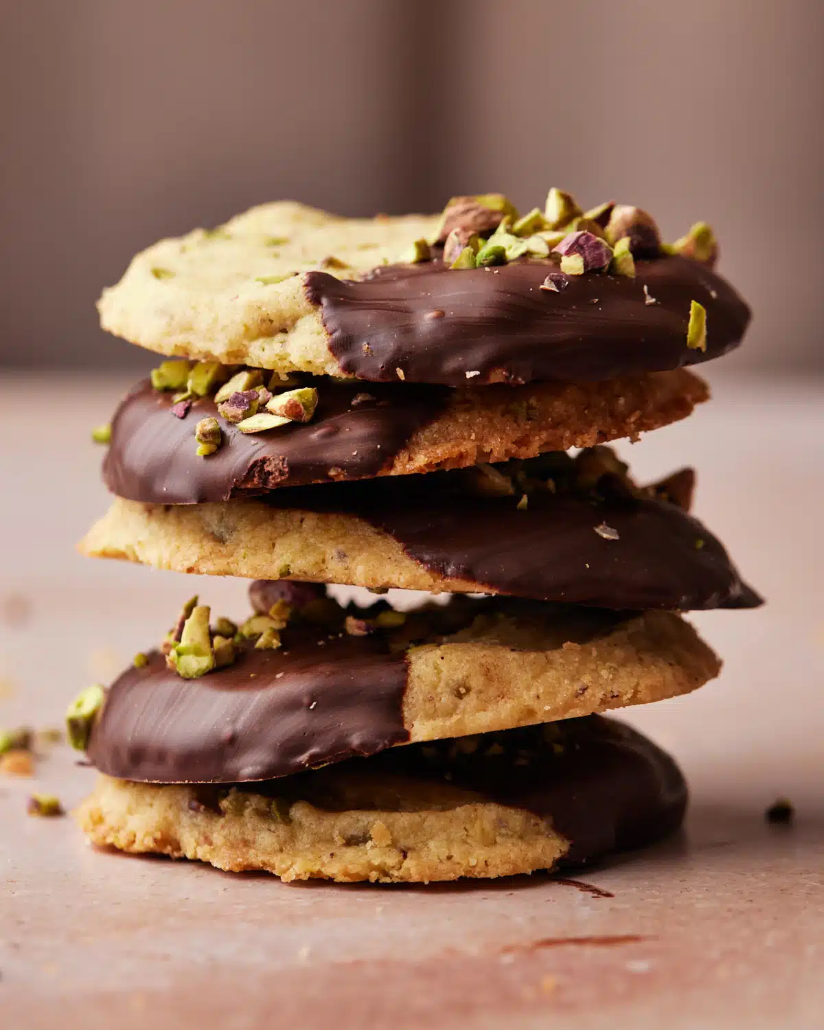 Chocolate-dipped pistachios shortbread cookies stacked up in a pile.