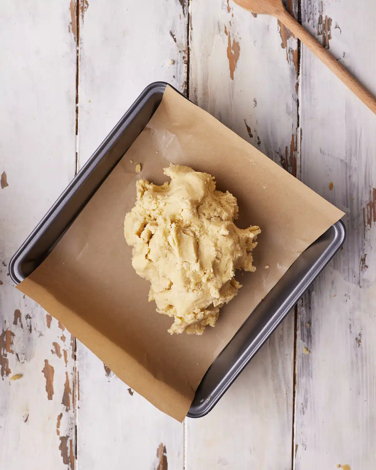 Shortbread dough being placed in a square baking pan.