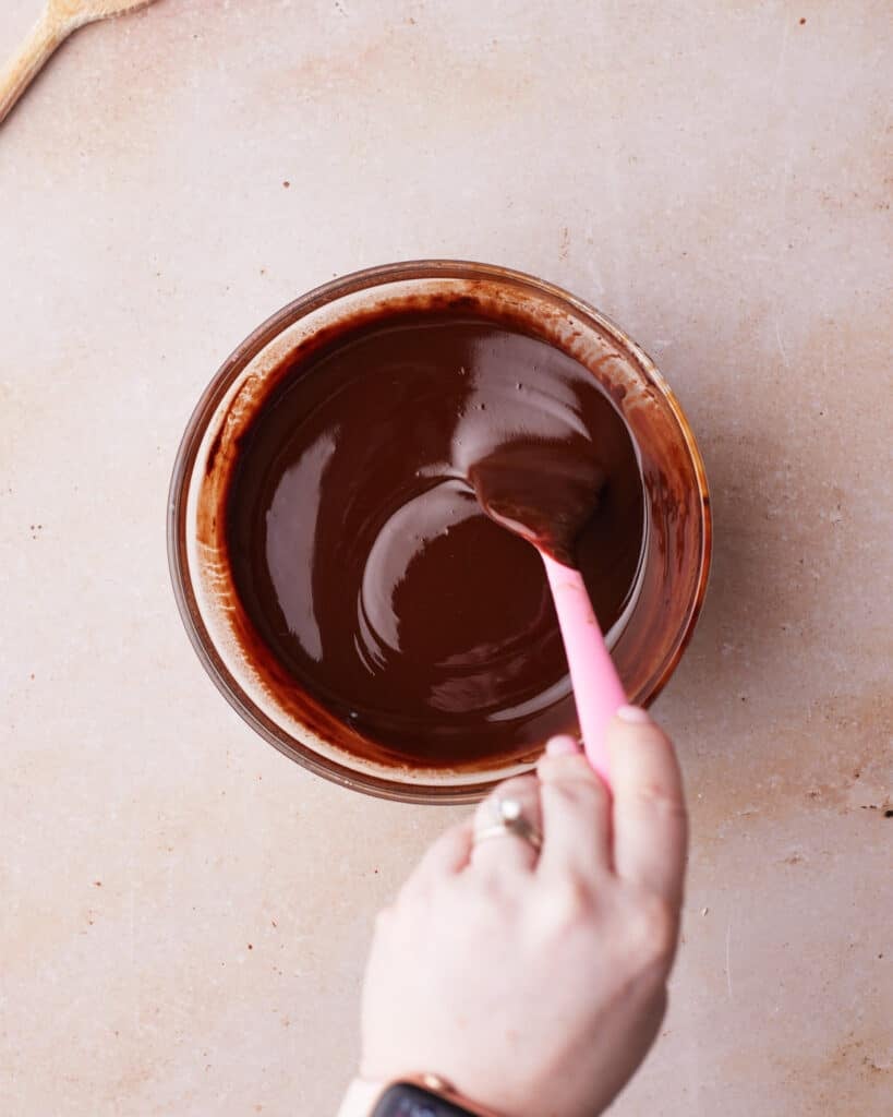 Chocolate and butter melted together in a glass bowl, being stirred.