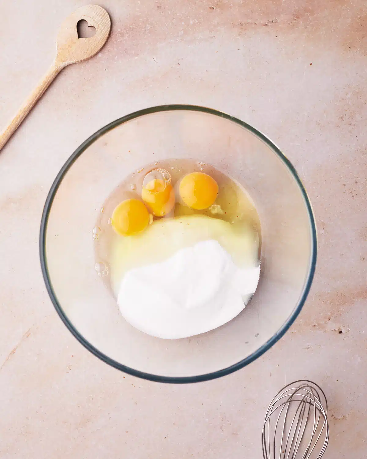 Eggs and sugar in a glass mixing bowl.