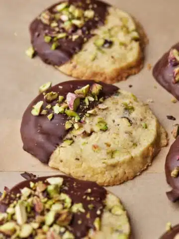 Round pistachio shortbread cookies in a row, dipped in chocolate and topped with chopped pistachios.