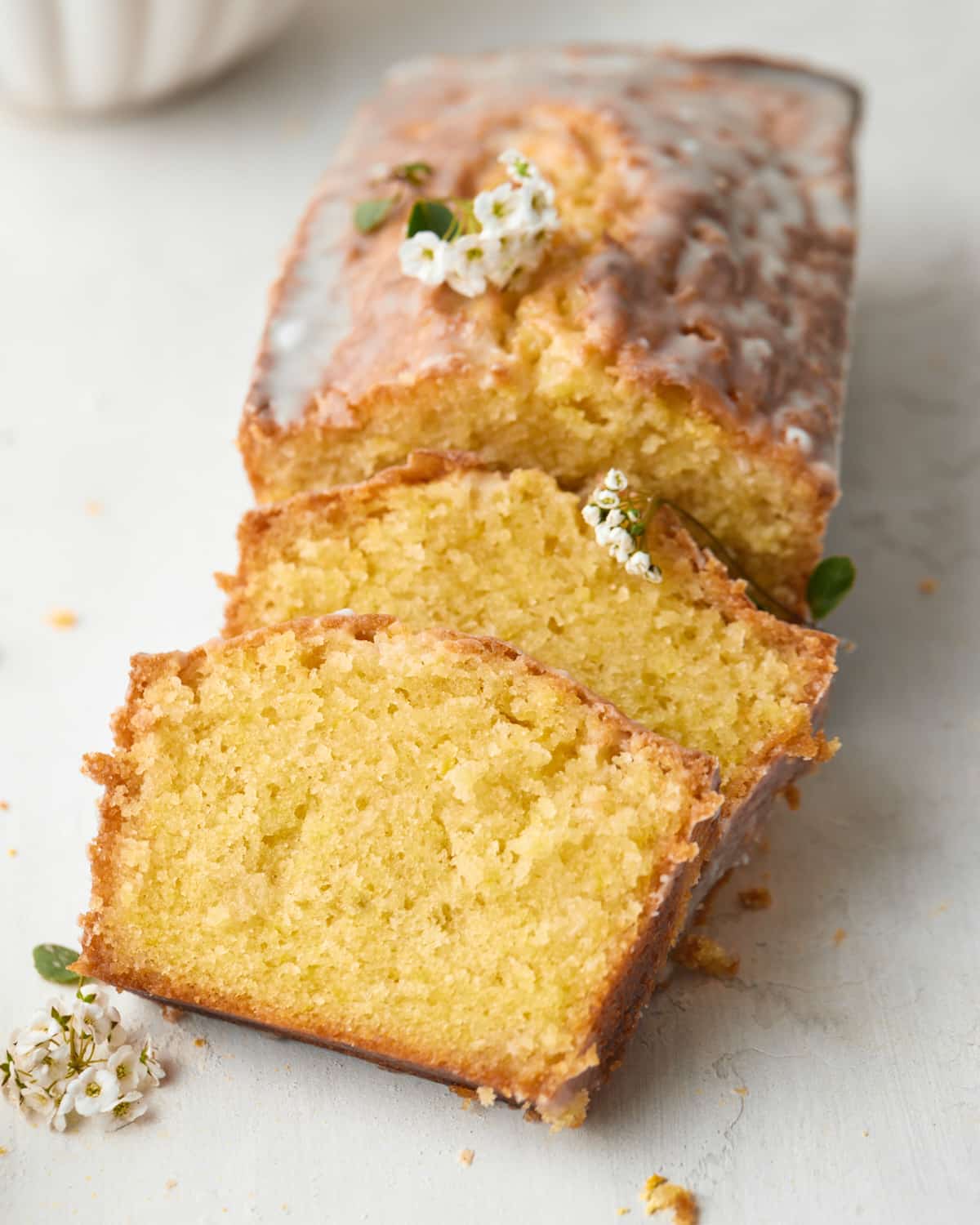 Lemon Drizzle Cake on a white table, two slices have been cut out of the loaf and are propped up on the side. 