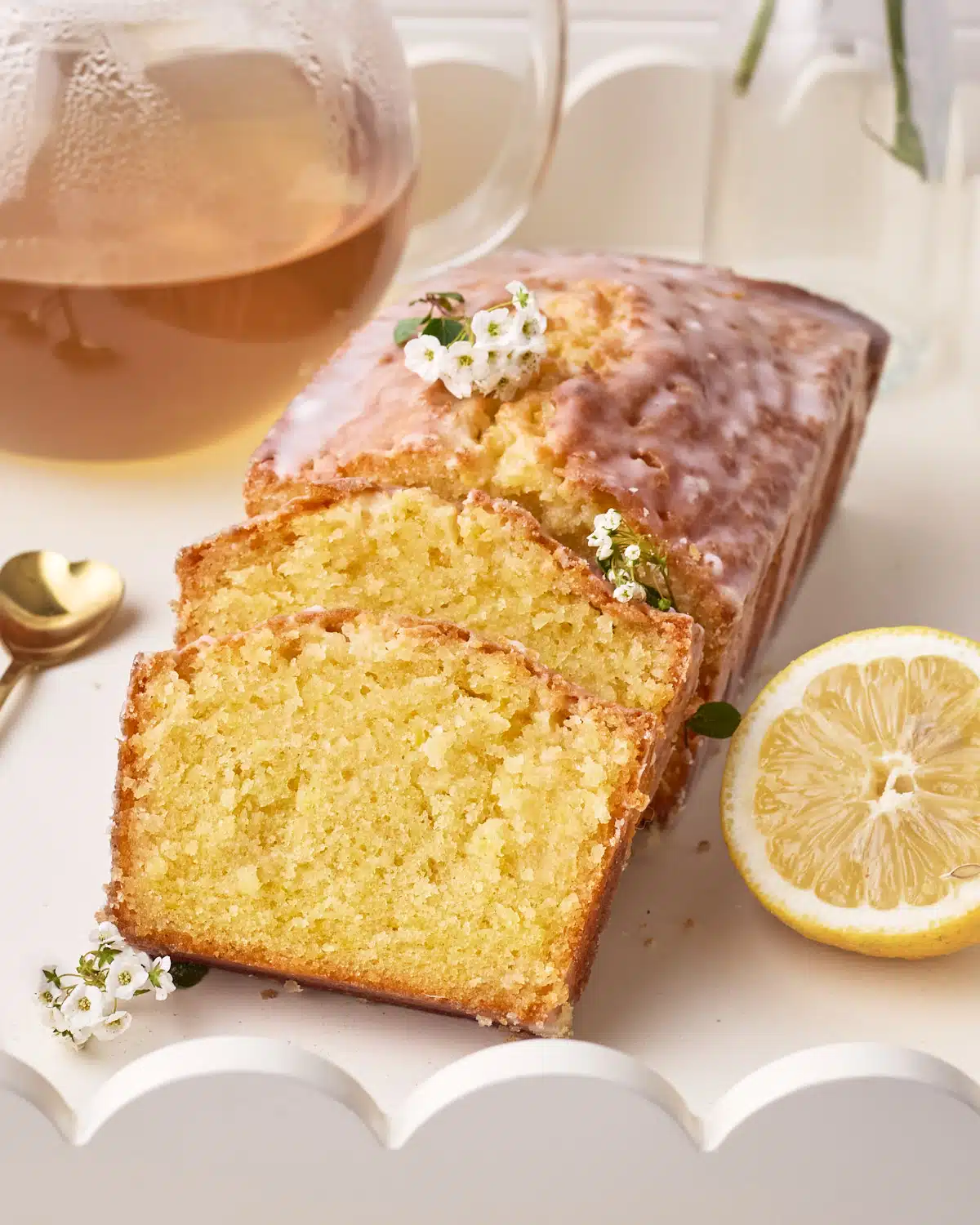 Lemon Drizzle Cake on a white serving tray with two slices sloping against the side, a fresh slice of lemon next to it.