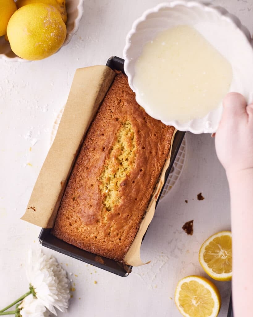 Pouring lemon glaze over the top of a lemon loaf to make lemon drizzle cake.