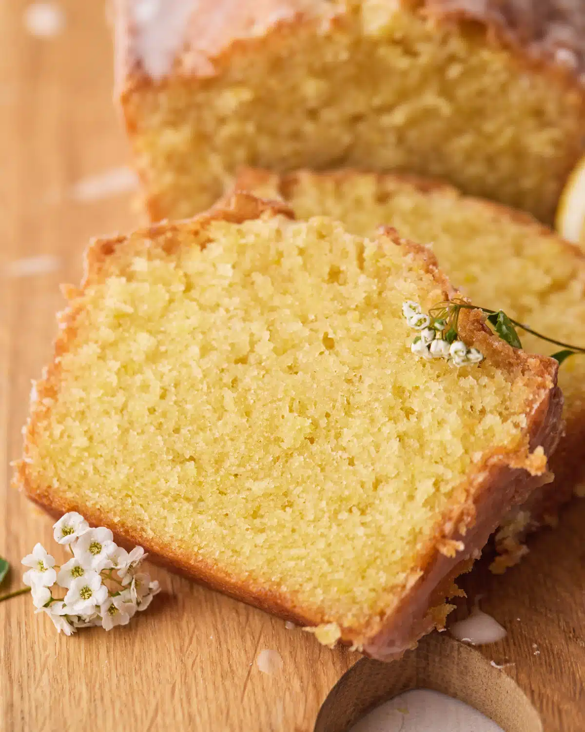 Close up of a slice of lemon drizzle cake with some fresh white garden flowers on top. 
