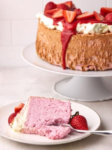 Pink Strawberry angel food cake with a slice taken out, the slice is sitting on a place in front with fresh strawberries.