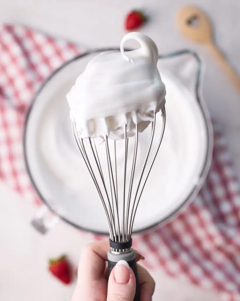Meringue on a balloon whisk, whipped to stiff peaks.