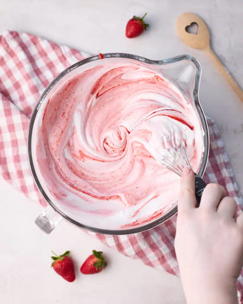 Strawberry puree being mixed into meringue with a whisk to make strawberry angel food cake.