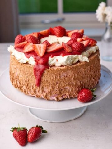 Strawberry angel food cake on a white cake plate, with whipped cream and fresh strawberries on top,