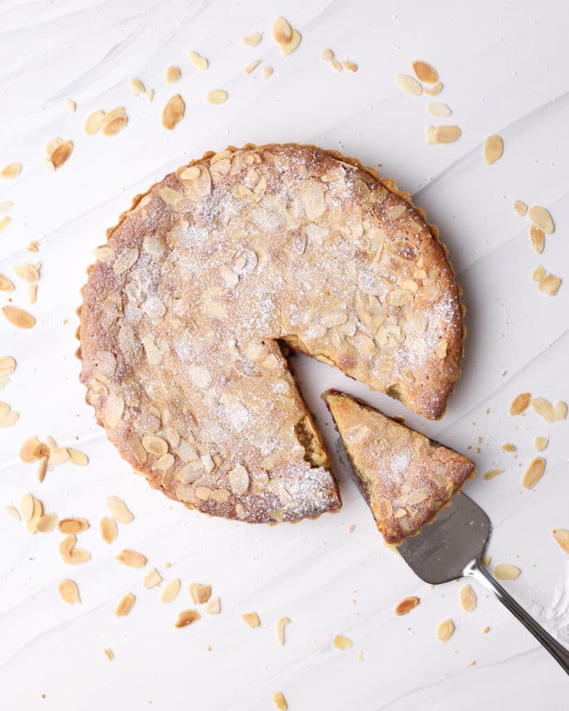 Overhead view of a bakewell tart with a slice being taken out of it. 