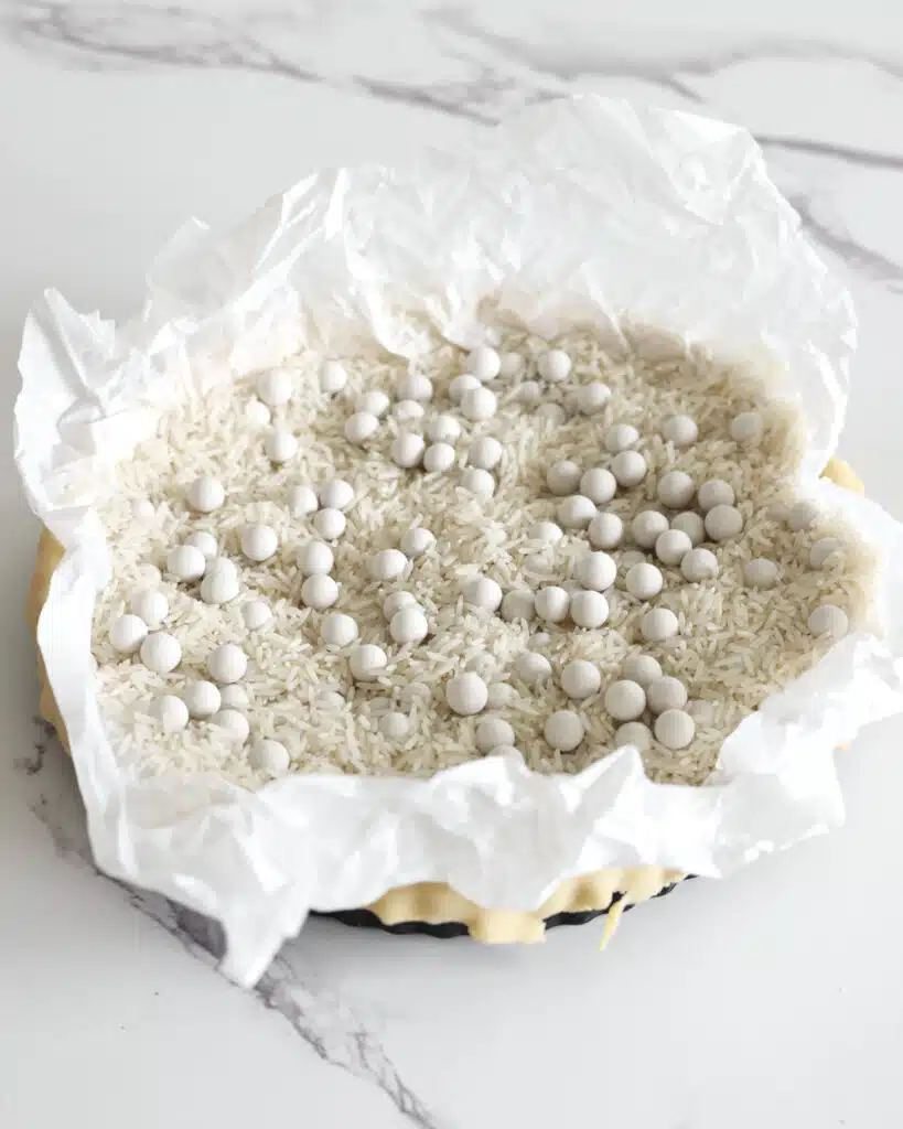 Filling a tart pan with pie weights to blind bake the pastry.