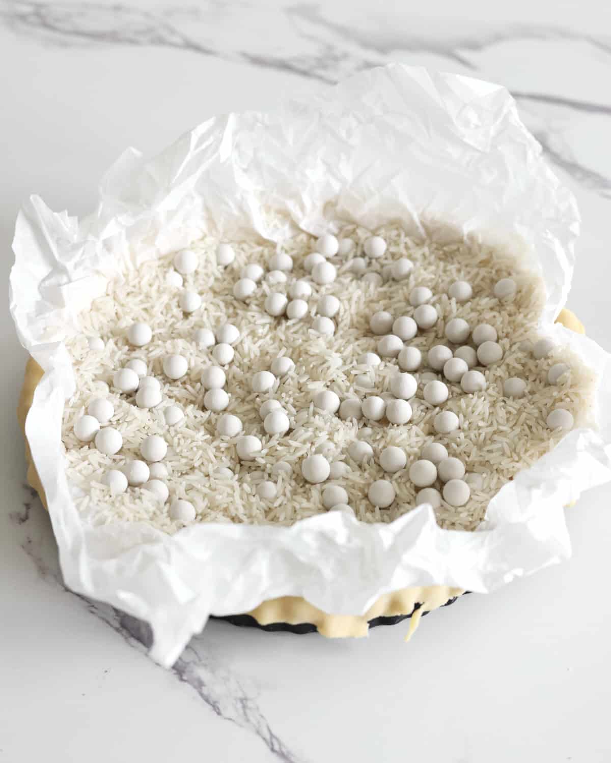 Filling a tart pan with pie weights to blind bake the pastry.