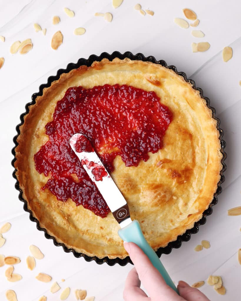 Spreading raspberry jam into a tart case to make bakewell tart. 