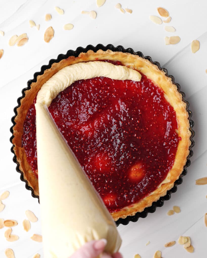 Piping frangipane into a pastry case on top of raspberry jam to make a bakewell tart. 