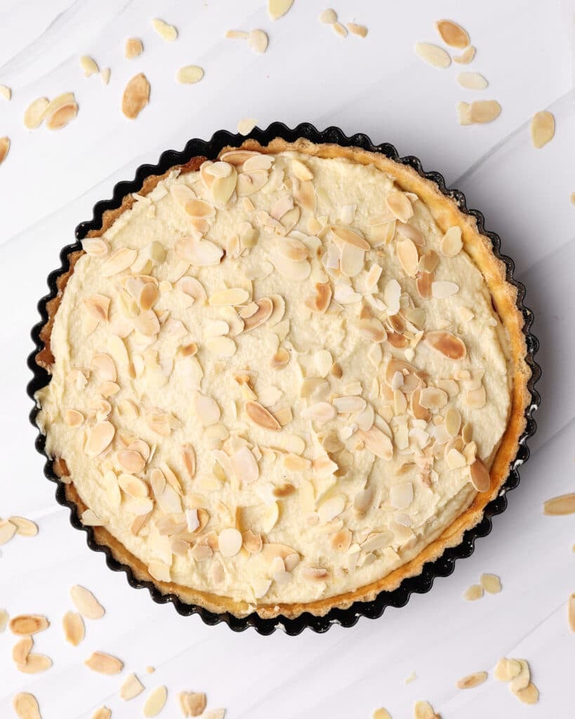 Flaked almonds being sprinkled on top of a bakewell tart before baking. 