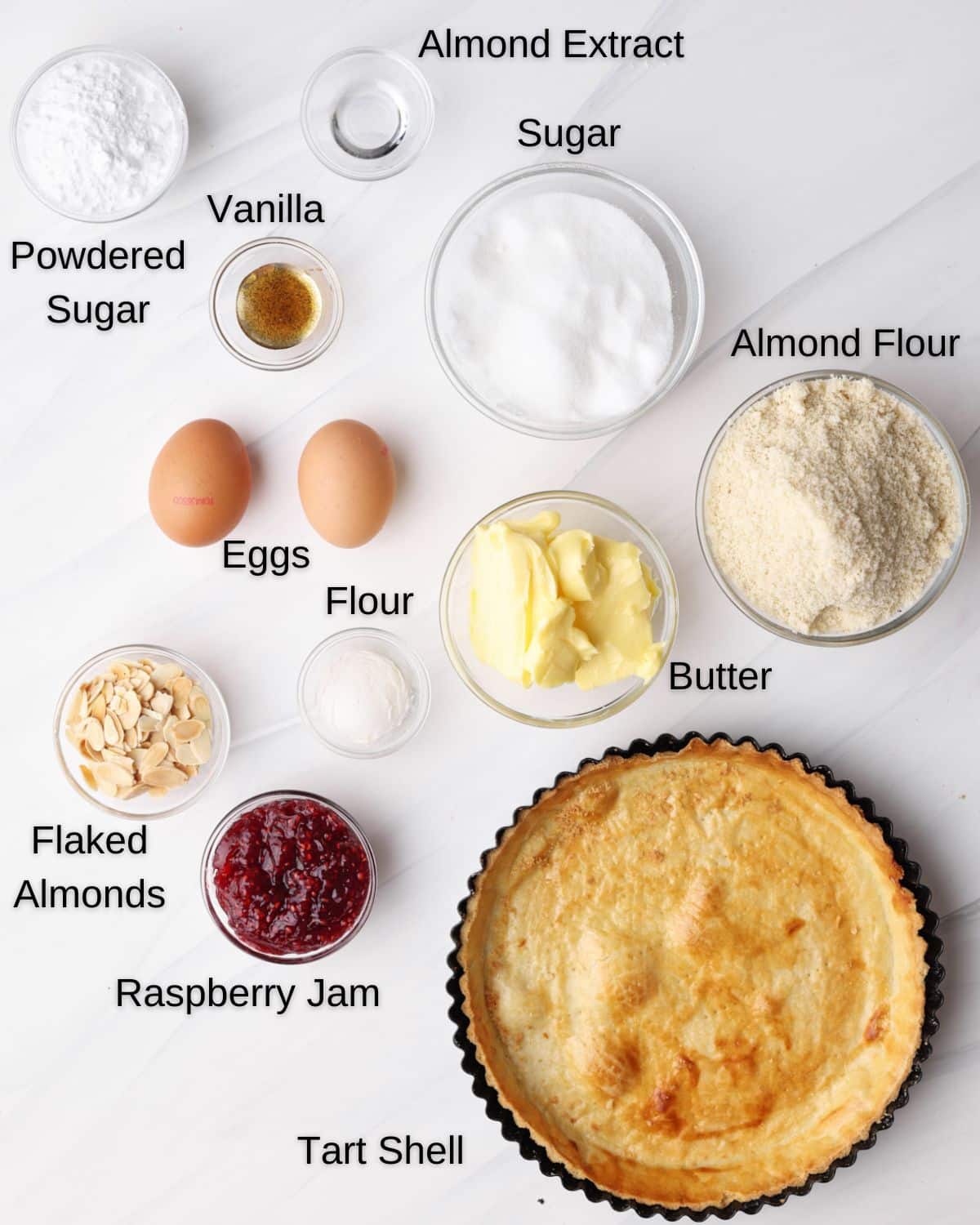 Ingredients to make bakewell tart - tart shell, almond meal, raspberry jam, sugar, flour, butter, eggs, vanilla, almond extract, flaked almonds, powdered sugar. 