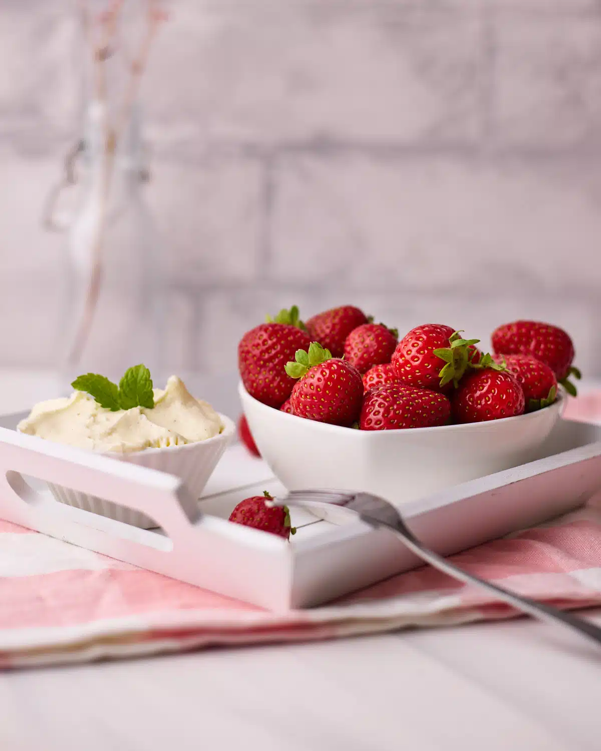 Large bowl filled with fresh strawberries and a smaller bowl with chantilly cream, all on a small wooden platter. 