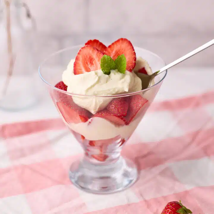Glass dish filled with layers of fresh strawberries and cream, topped with fresh mint leaves.