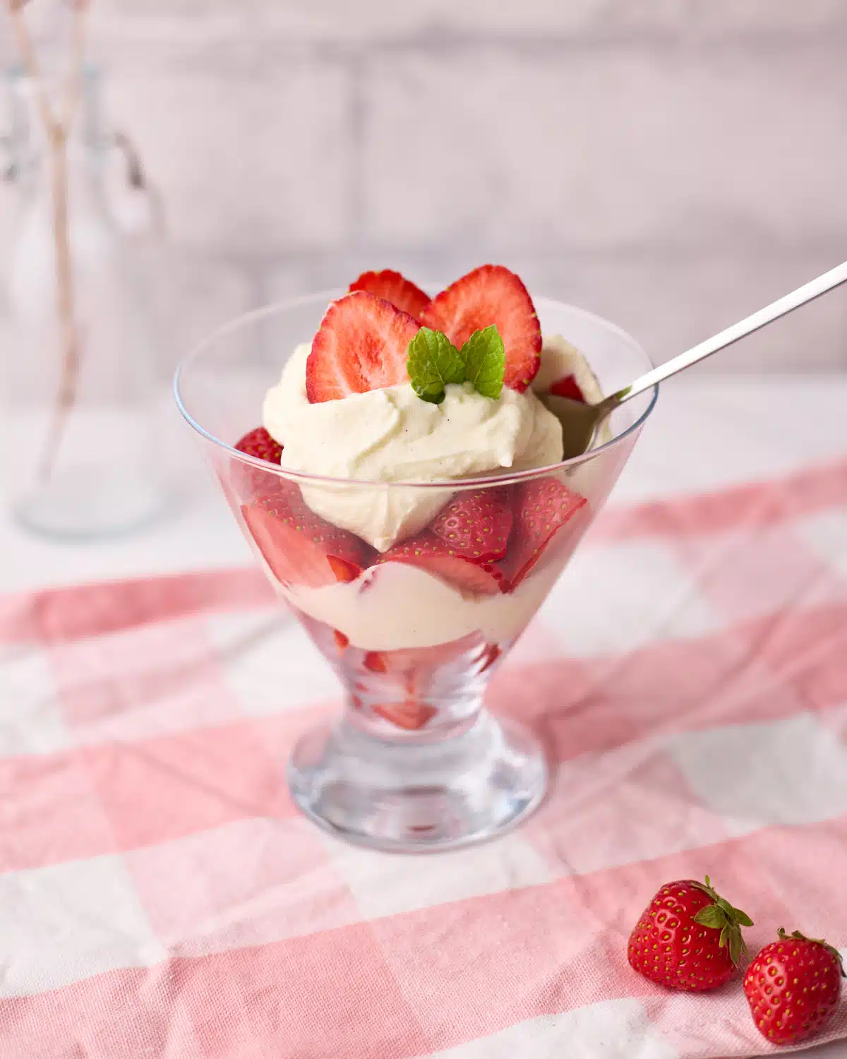 Glass dish filled with layers of fresh strawberries and cream, topped with fresh mint leaves.