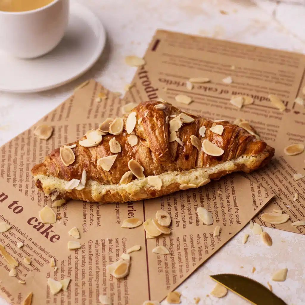 almond croissant on some brown paper next to a small cup of espresso.