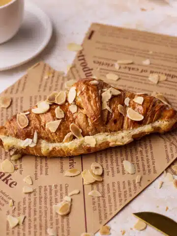 almond croissant on some brown paper next to a small cup of espresso.